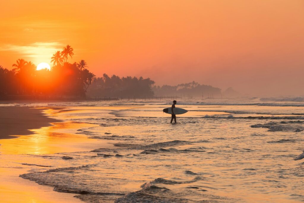 Silhouette di un surfista che cammina verso l'oceano durante il tramonto