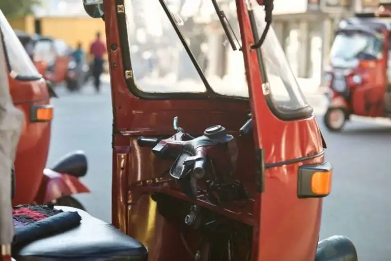 Red tuk tuk parked against busy street. Popular three wheeled motorcycle in Sri Lanka.